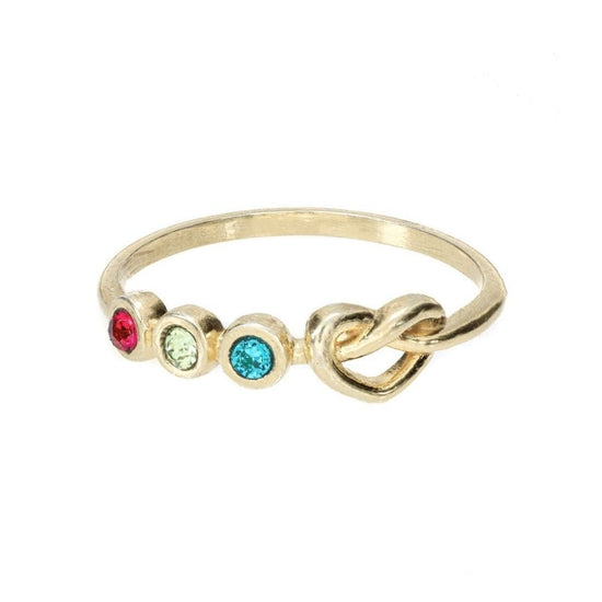 Anillo dorado personalizado Lazos del corazón con tres piedras redondas de nacimiento -roja, verde claro y azul- en hilera junto a un pequeño nudo en la banda, sobre un fondo blanco liso.