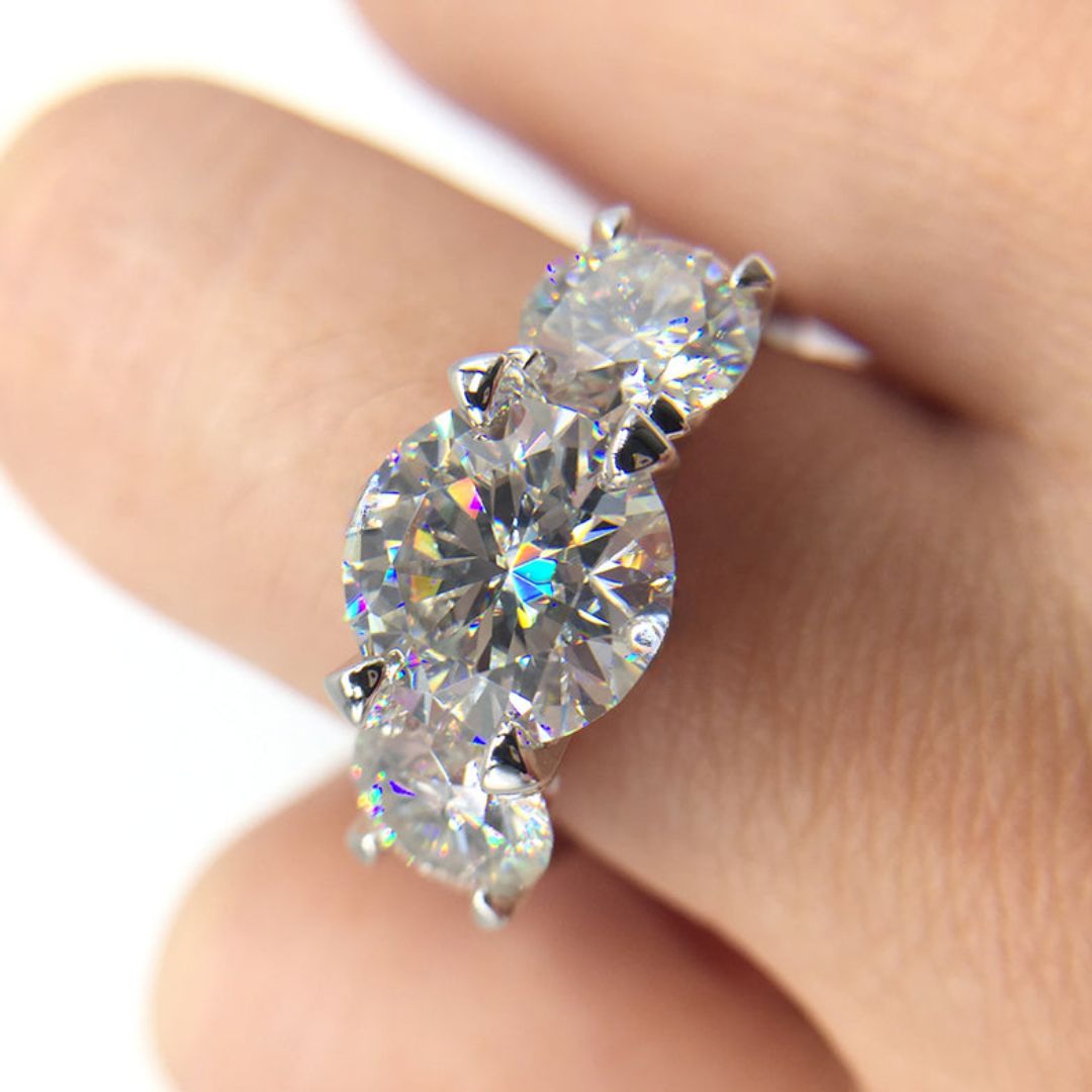 Primer plano de una mano que luce el Anillo Tres destellos de amor, con tres grandes circonitas redondas brillantes engastadas en acero inoxidable, siendo la piedra central la más grande.