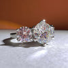 Primer plano del Anillo Tres destellos de amor, elaborado en plata con tres piedras redondas brillantes -una prominente en el centro y dos más pequeñas a cada lado- engastadas sobre un suave fondo naranja y blanco.