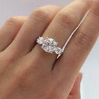 Una mano luce el Anillo Tres destellos de amor, un anillo de acero inoxidable con un gran diamante central redondo y diamantes laterales más pequeños, sobre un fondo claro.