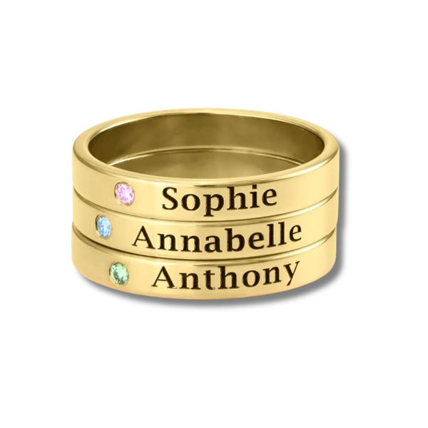 Tres anillos apilables con nombres y piedras de nacimiento, grabados con Sophie, Annabelle y Anthony. Cada anillo tiene una gema única junto al nombre.