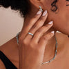 Una persona de piel morena clara lleva un ear cuff de plata retorcida, un collar de cadena y un Anillo apilable con nombre y piedra de nacimiento grabado con ESCORPIO en el dedo, mientras sus uñas pulcramente cuidadas tocan suavemente su oreja.