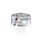 Tres Anillos apilables con nombres y piedras de nacimiento exhiben "Sebastian" (rojo), "Elijah" (transparente) y "Emilia" (verde); cada uno con su nombre grabado y piedra correspondiente.