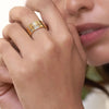 Una mano femenina cerca de los labios luce tres anillos apilables con nombres grabados y piedras de nacimiento; el rostro es parcialmente visible y la piel se ve suave y natural.