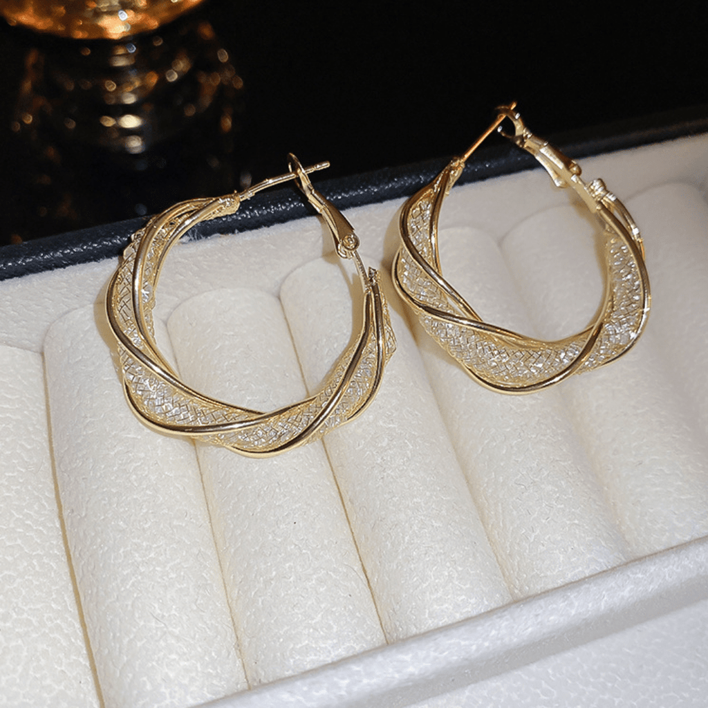 Aretes colgantes en espiral, hechos de acero inoxidable dorado con detalles brillantes, se muestran sobre una bandeja para joyas color crema con borde negro.
