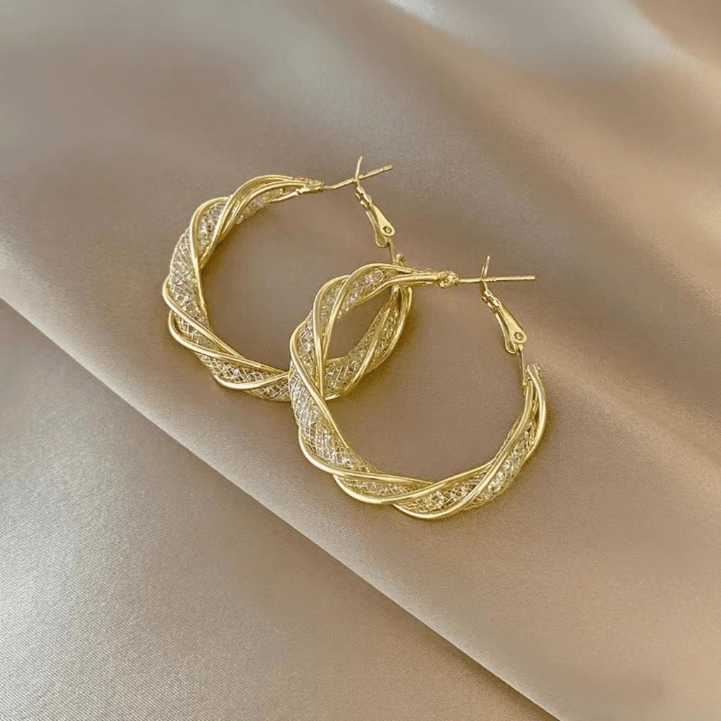 Aretes colgantes en espiral, elaborados en acero inoxidable dorado, sobre fondo de satén color oro claro.