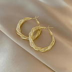 Aretes colgantes en espiral, elaborados en acero inoxidable dorado, sobre fondo de satén color oro claro.
