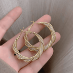 Una mano sujeta Aretes colgantes en espiral, con aros de oro retorcidos con un brillante diseño de celosía en tonos dorados y plateados mezclados, elaborados en acero inoxidable dorado para un aspecto texturizado y elegante.