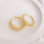 Aretes colgantes en espiral hechos de acero inoxidable dorado, con diseño retorcido y textura brillante, reposan sobre un plato de cerámica blanca.