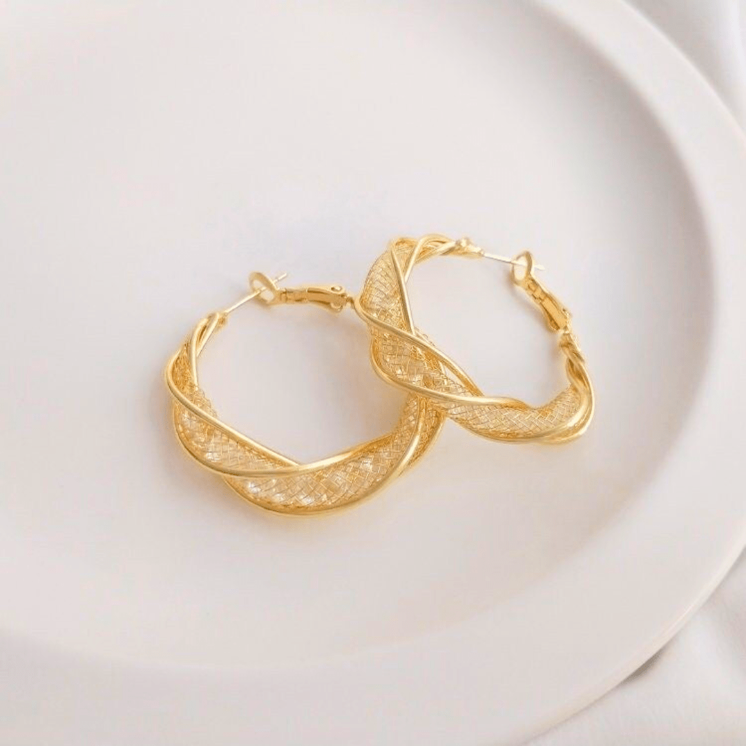 Aretes colgantes en espiral hechos de acero inoxidable dorado, con diseño retorcido y textura brillante, reposan sobre un plato de cerámica blanca.