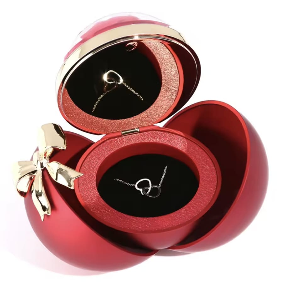 Una Caja Corazón con rosa eterna y collar corazón personalizado, con un lazo dorado y un interior negro-rojo, que presenta con elegancia el collar personalizado, un regalo ideal para ocasiones especiales.