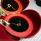 Un collar de corazón personalizado con un colgante de oro se exhibe en la Caja Corazón, que presenta una rosa eterna y descansa dentro de un joyero rojo con forma de manzana forrado con tela negra y roja para una presentación encantadora.