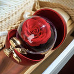 La Caja Corazón con rosa eterna y collar corazón personalizado presenta una rosa preservada en una cúpula transparente, colocada en una caja roja en forma de corazón con un lazo dorado, perfecta para regalar.