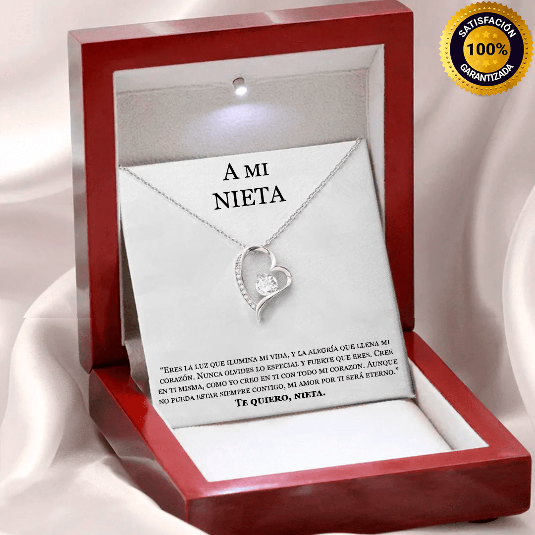 El collar Amor eterno es un collar de plata en forma de corazón con un colgante de cristal, presentado en un joyero rojo. La tapa interior reza A MI NIETA con un cariñoso mensaje, además de un distintivo dorado 100% satisfacción garantizada en la esquina superior derecha.