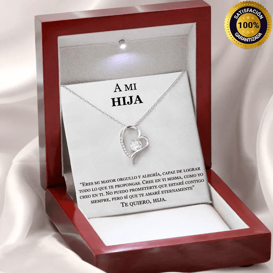 El collar Amor eterno de plata con forma de corazón y una piedra brillante se presenta en un joyero rojo con una sentida dedicatoria en español "A MI HIJA" y un sello dorado "100% satisfacción garantizada".