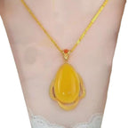 El collar amuleto de piedra ágata amarilla, con colgante en forma de lágrima y marco de oro detallado, irradia energía positiva y elegancia, presentado sobre un busto de maniquí.