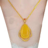 El collar amuleto de piedra ágata amarilla, con colgante en forma de lágrima y marco de oro detallado, irradia energía positiva y elegancia, presentado sobre un busto de maniquí.