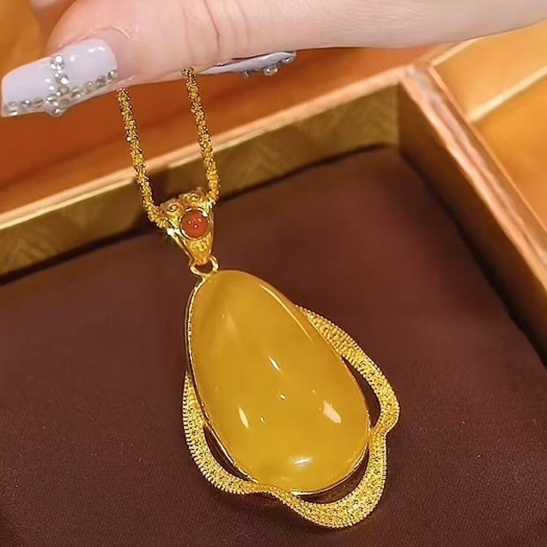 Una mano cuidada sostiene el Collar amuleto de piedra ágata amarilla, un collar retro con una gran piedra de ágata amarilla en forma de lágrima, que irradia energía positiva sobre un fondo de tela marrón oscuro.