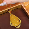 Una mano cuidada sostiene el Collar amuleto de piedra ágata amarilla, un collar retro con una gran piedra de ágata amarilla en forma de lágrima, que irradia energía positiva sobre un fondo de tela marrón oscuro.