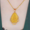 El collar amuleto de piedra ágata amarilla luce un gran dije ovalado enmarcado en oro texturizado y una pequeña piedra naranja, irradiando energía positiva sobre piel clara con prendas verde oscuro.