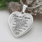 El collar con colgante "Para mi esposa", en forma de corazón plateado y grabado en español con un mensaje conmovedor, reposa sobre una piedra junto a hojas verdes, ideal como regalo especial de amor.