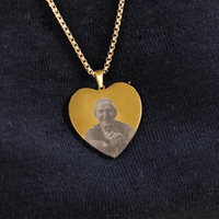 El Collar con foto grabada en forma de corazón muestra un retrato elegante de una persona mayor, posando sobre tela oscura y texturizada.