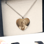 El Collar con foto grabada en forma de corazón es de plata e incluye el retrato grabado de una mujer mayor con gafas y cabello rizado, presentado en un estuche joyero con forro de tela clara.
