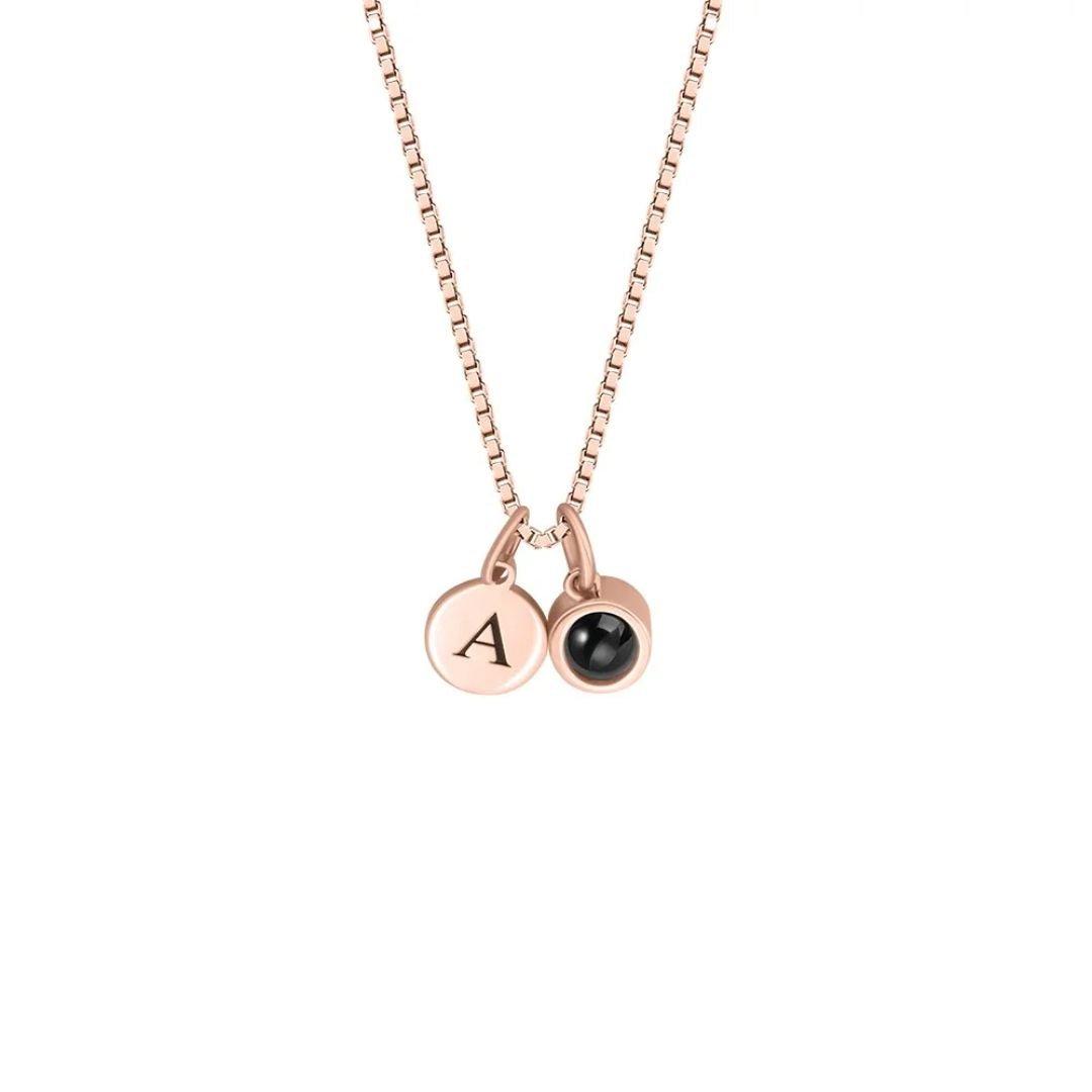 Collar con inicial y foto en oro rosa con dos dijes redondos: uno grabado con la letra A y otro decorado con una pequeña gema negra.