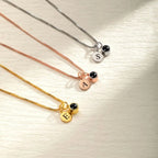 Tres collares con acabados en plata, oro rosa y oro, cada uno con un pequeño colgante redondo de cuenta negra y un colgante redondo grabado con una S, una A o una E, igual que el Collar con inicial y foto.