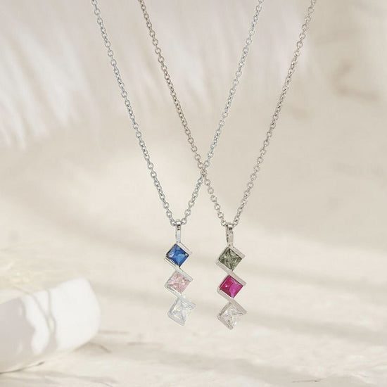 El collar con múltiples piedras de nacimiento en color plateado luce dos dijes cuadrados apilados, perfecto como collar personalizado para mamá, ideal para regalo, mostrado sobre un fondo neutro y claro.