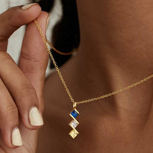 Cargar imagen en el visor de la galería, Una persona sostiene un Collar con múltiples piedras de nacimiento en oro personalizado, con tres gemas cuadradas-azul, transparente y amarilla-colgando en vertical. Se ven su piel y uñas claras. Regalo ideal para mamá.