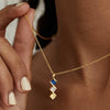 Una persona sostiene un Collar con múltiples piedras de nacimiento en oro personalizado, con tres gemas cuadradas-azul, transparente y amarilla-colgando en vertical. Se ven su piel y uñas claras. Regalo ideal para mamá.