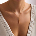 Una persona lleva un top de punto crema con un profundo escote y un delicado collar dorado con múltiples piedras de nacimiento, con cinco coloridas piedras de nacimiento en un colgante vertical-perfecto como regalo para mamá.