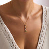 Una persona lleva un top de punto crema con un profundo escote y un delicado collar dorado con múltiples piedras de nacimiento, con cinco coloridas piedras de nacimiento en un colgante vertical-perfecto como regalo para mamá.