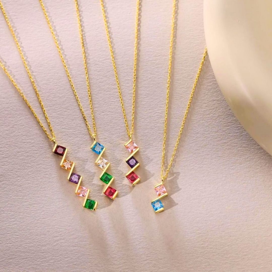 Cinco collares de oro, cada uno con un colgante rectangular de piedra de nacimiento en rojo, azul, verde, morado o rosa. El Collar con múltiples piedras de nacimiento es un regalo personalizado ideal para mamá.