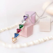 Cargar imagen en el visor de la galería, El Collar con piedras de nacimiento personalizadas presenta un dije vertical con seis gemas de colores en línea-amarillo, azul, rojo, verde, transparente y lila-ideal como regalo para mamá. Se muestra sobre fondo rosa suave y beige.