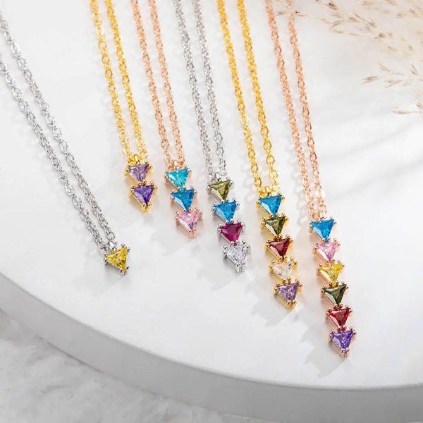 El collar con piedras de nacimiento personalizadas en dorado es un regalo ideal para mamá o como collar de piedras de nacimiento, presentando colgantes triangulares sobre una superficie blanca.