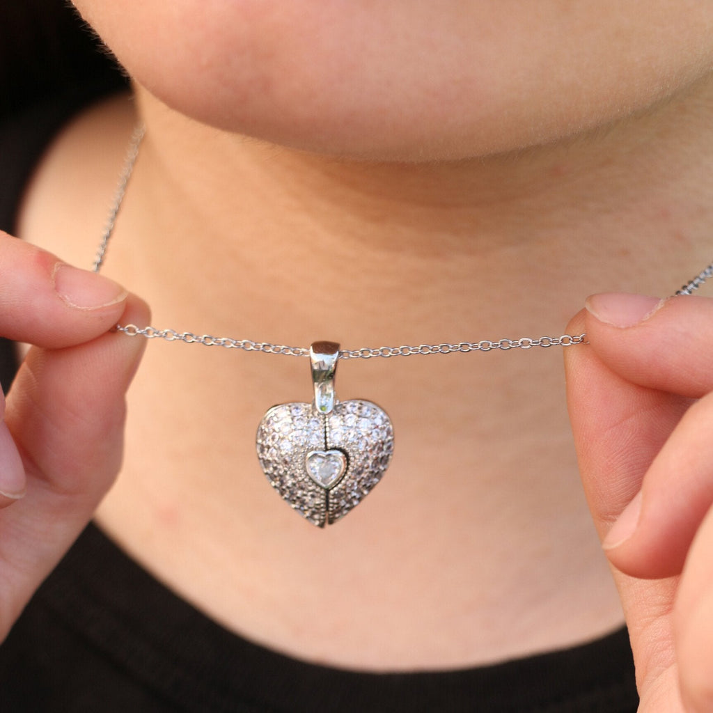 Una persona sostiene cerca del cuello el Collar Corazón con alas de ángel y foto, un collar de plata con un colgante en forma de corazón con alas de ángel y espacio para una foto personalizada.