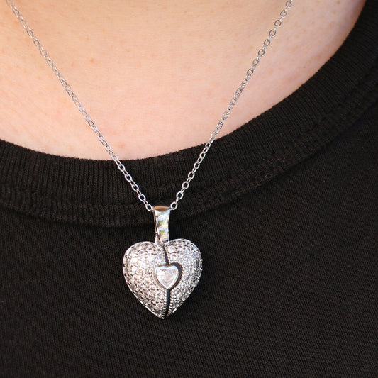Primer plano de un collar de plata con colgante Corazón con alas de ángel y foto, que se lleva sobre una camisa negra. La delicada cadena y el diseño de corazón alado aportan un toque de elegancia y brillo al look.