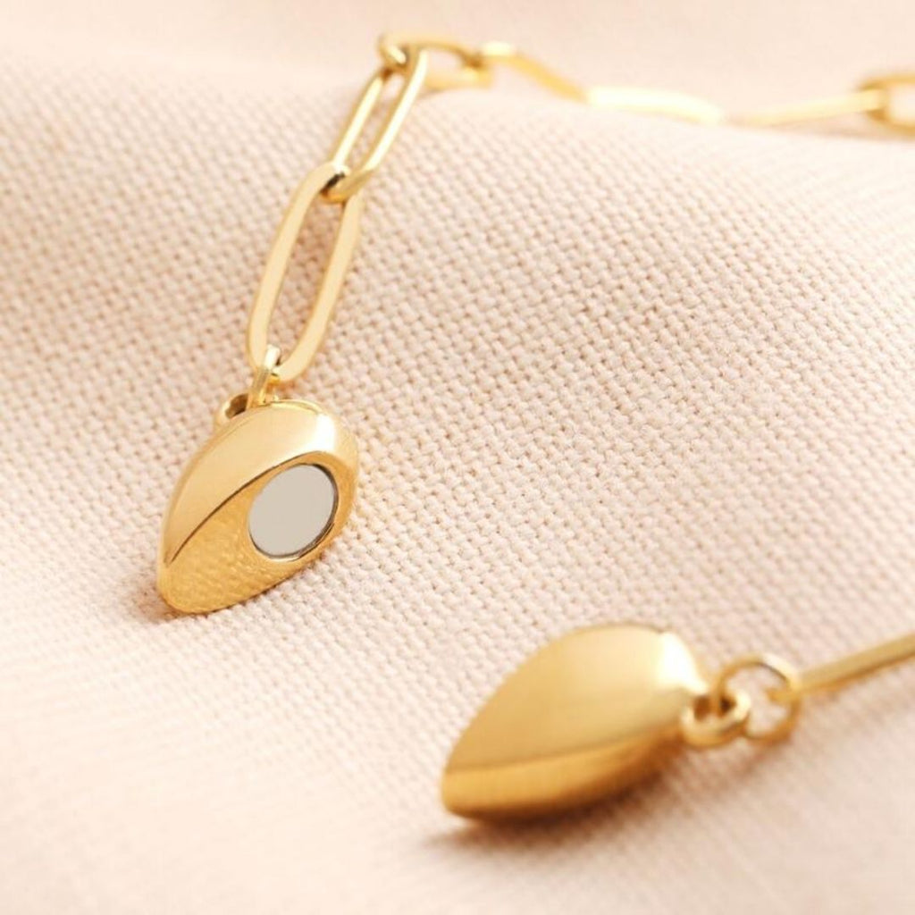 Primer plano de dos collares de oro Collar Corazón Magnético, ideales como collar de pareja o regalo de San Valentín, con colgantes de corazón magnético de forma ovalada -uno de espejo- sobre tela beige texturizada.