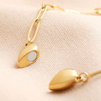 Primer plano de dos collares de oro Collar Corazón Magnético, ideales como collar de pareja o regalo de San Valentín, con colgantes de corazón magnético de forma ovalada -uno de espejo- sobre tela beige texturizada.