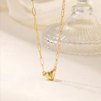 El collar Corazón magnético presenta eslabones alargados de oro y un colgante de corazón facetado, ideal como collar de pareja o regalo de San Valentín. Se muestra sobre un fondo neutro con un adorno de cristal en la distancia.