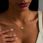 Una mujer luce el Collar Corazón magnético, un collar dorado con dije de corazón, combinando con una blusa blanca. Su mano cerca del cuello resalta el collar, perfecto como regalo de San Valentín o collar de pareja.