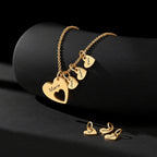 El collar Corazones de familia presenta colgantes de oro en forma de corazón grabados con los nombres de María, Julia, Hubert y Lukas, además de pequeños colgantes de oro en forma de corazón sobre una superficie negra.