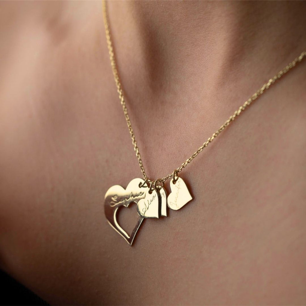 Detalle del collar Corazones de familia en el cuello de una persona, con un colgante en forma de corazón y dos pequeños dijes grabados, que lo convierten en el collar personalizado perfecto.