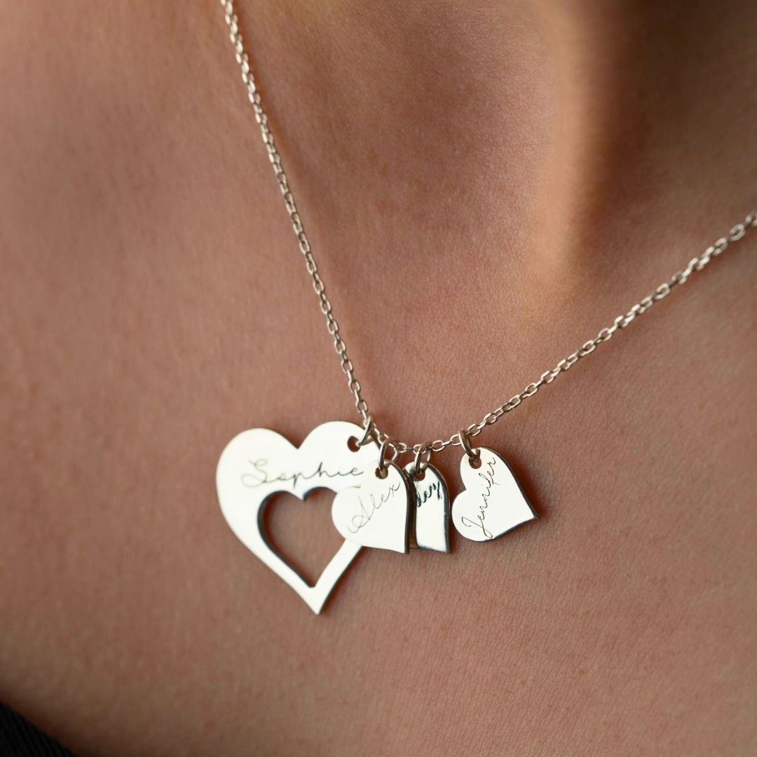 Primer plano del collar Corazones de familia, con cuatro colgantes en forma de corazón grabados con distintos nombres, apoyados en el cuello. Este elegante collar personalizado es ideal para tener cerca a sus seres queridos.