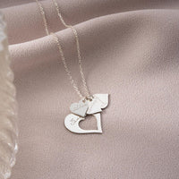 El collar Corazones de familia incluye tres colgantes en forma de corazón con elegantes grabados, expuestos sobre un suave tejido rosa, perfecto como regalo personalizado y lleno de significado.