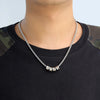 Una persona lleva una camiseta negra con parches de camuflaje en los hombros y un collar de cadena con dijes personalizados con cinco cuentas metálicas con texto grabado.