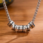 A Collar de cadena con dijes personalizados en plata, con seis cuentas cilíndricas grabadas con Fatima, JoseM, Toby, Penelope, 03-05-22 y Family sobre madera. Ideal como regalo Día del Padre o collar significativo con nombres.