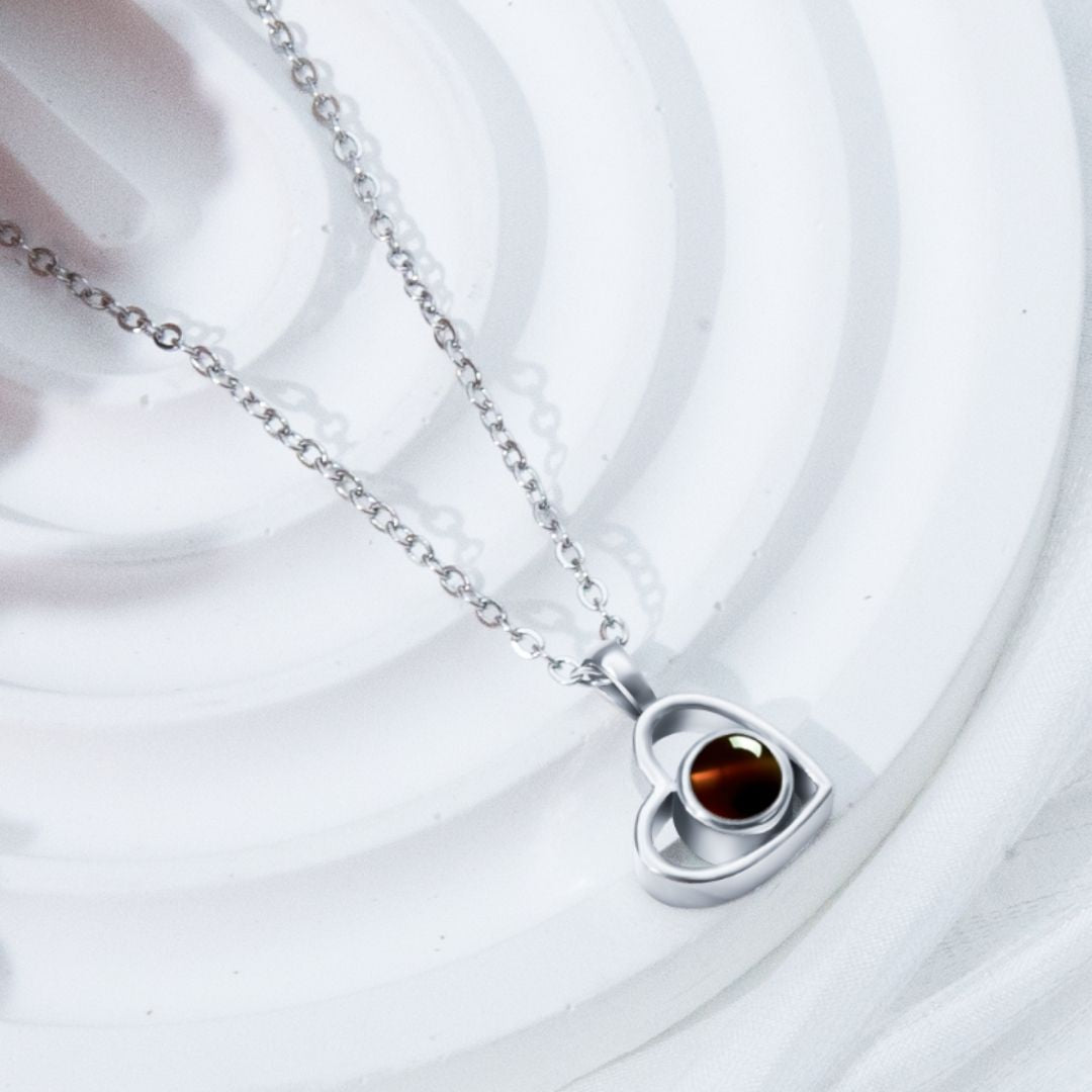 El Collar de corazón con foto, en color plateado, es ideal para collares personalizados y guardar recuerdos especiales. Presentado sobre un fondo blanco texturizado.